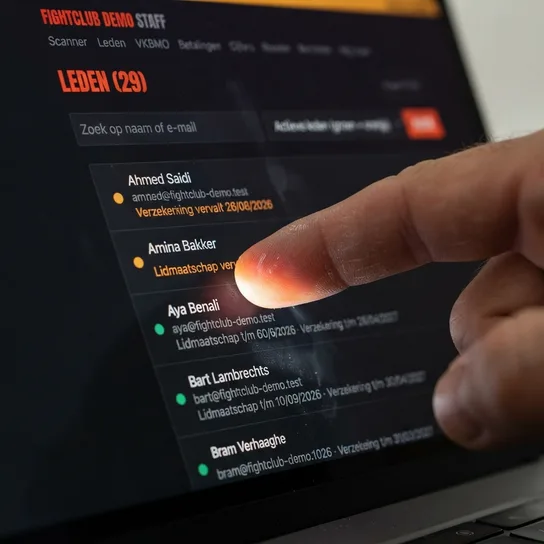 Vinger op een laptopscherm met de ledenlijst van Fightclub Demo: leden met een groene of oranje stip, hun e-mailadres en de vervaldatum eronder